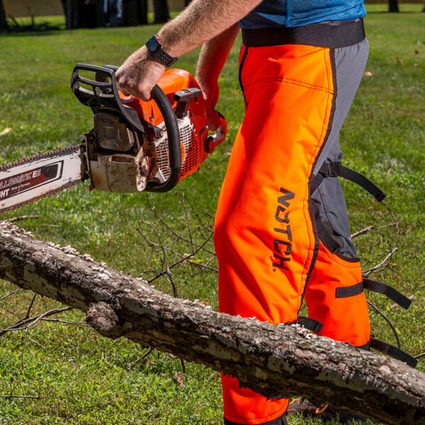 Man wearing chainsaw chaps cutting a tree.